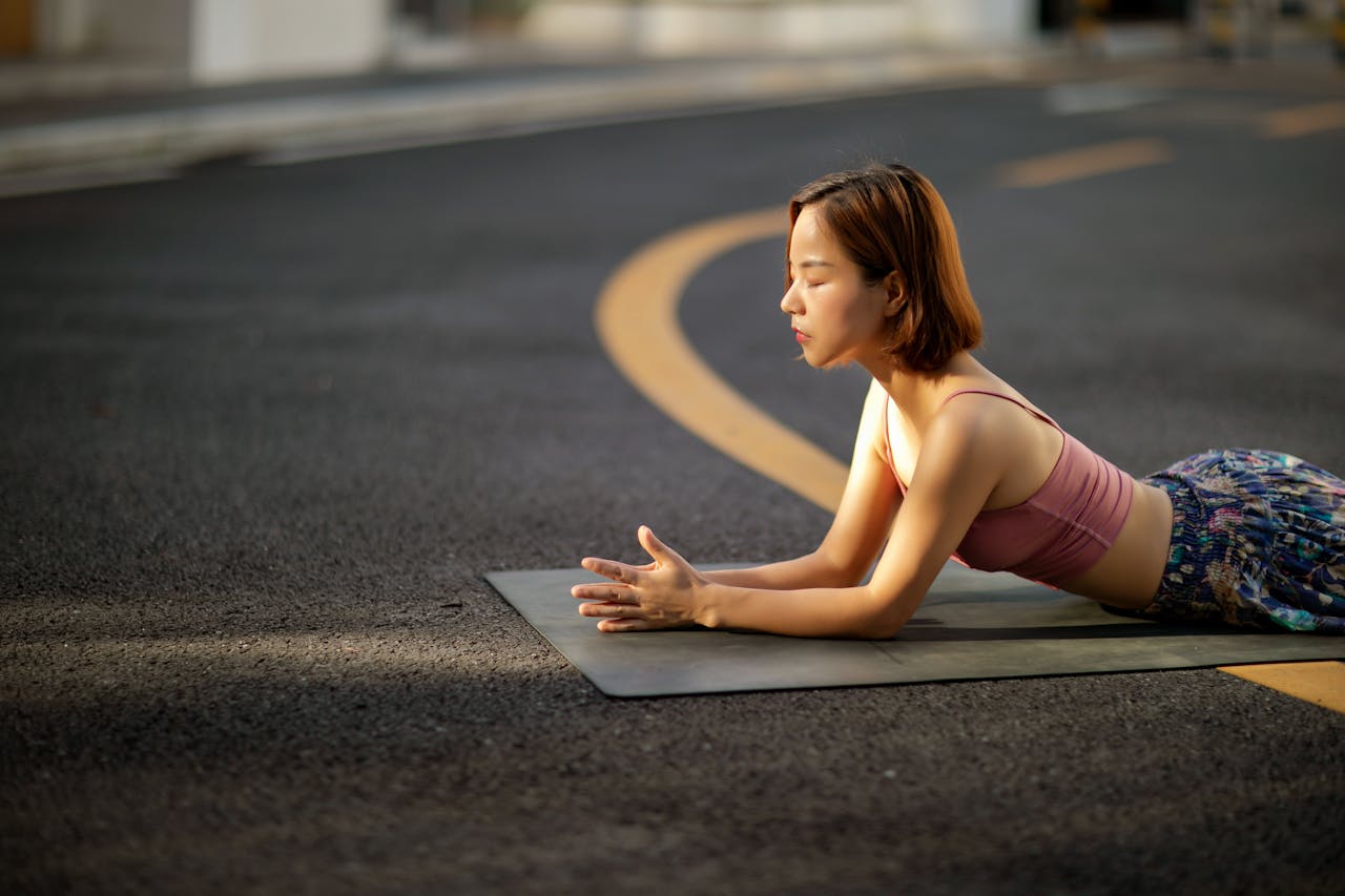 behind-the-scene-03 A woman meditating on a yoga mat in the middle of the road, enjoying peaceful outdoor exercise.