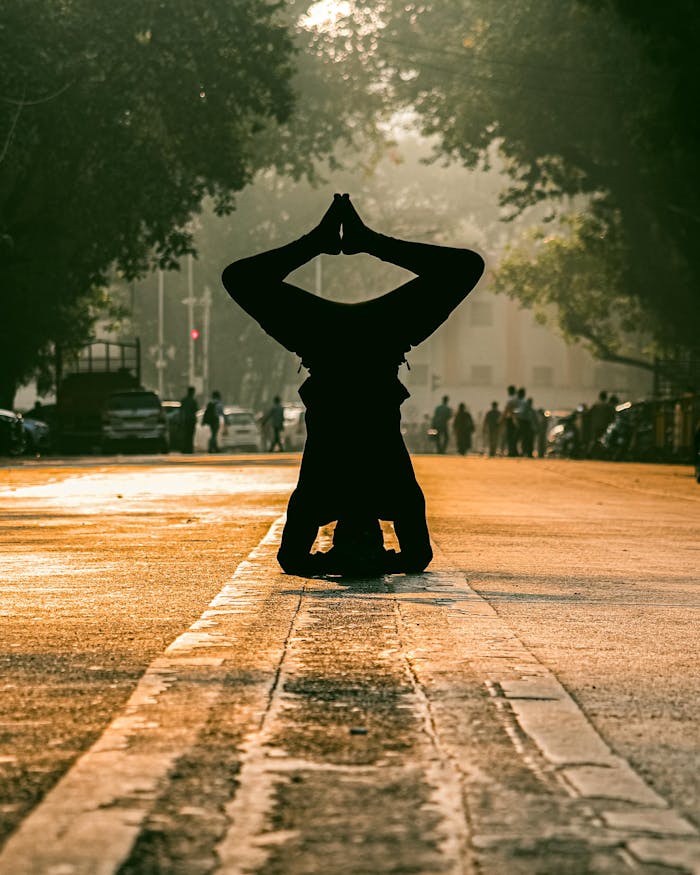 our-vission A person performs a headstand yoga pose on a sunlit Mumbai street, silhouetted at sunrise.