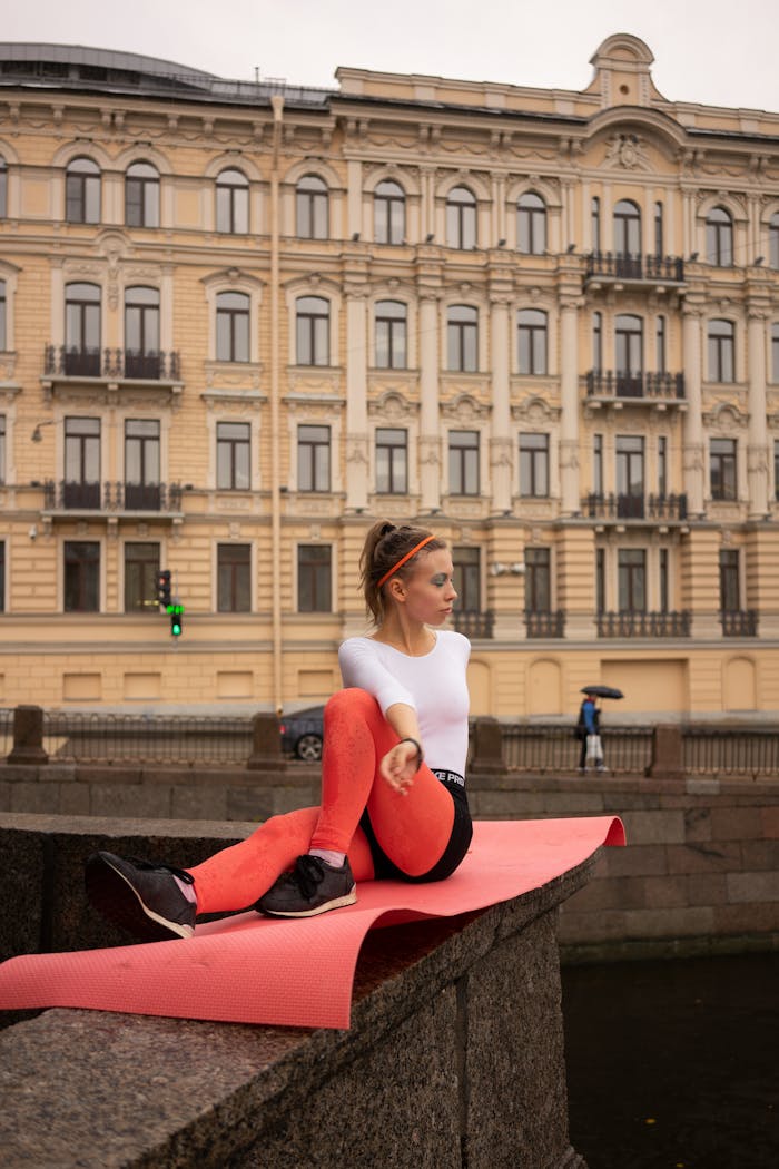 behind-the-scene-05 A woman in activewear practices yoga on a mat in front of a historic building in a city.